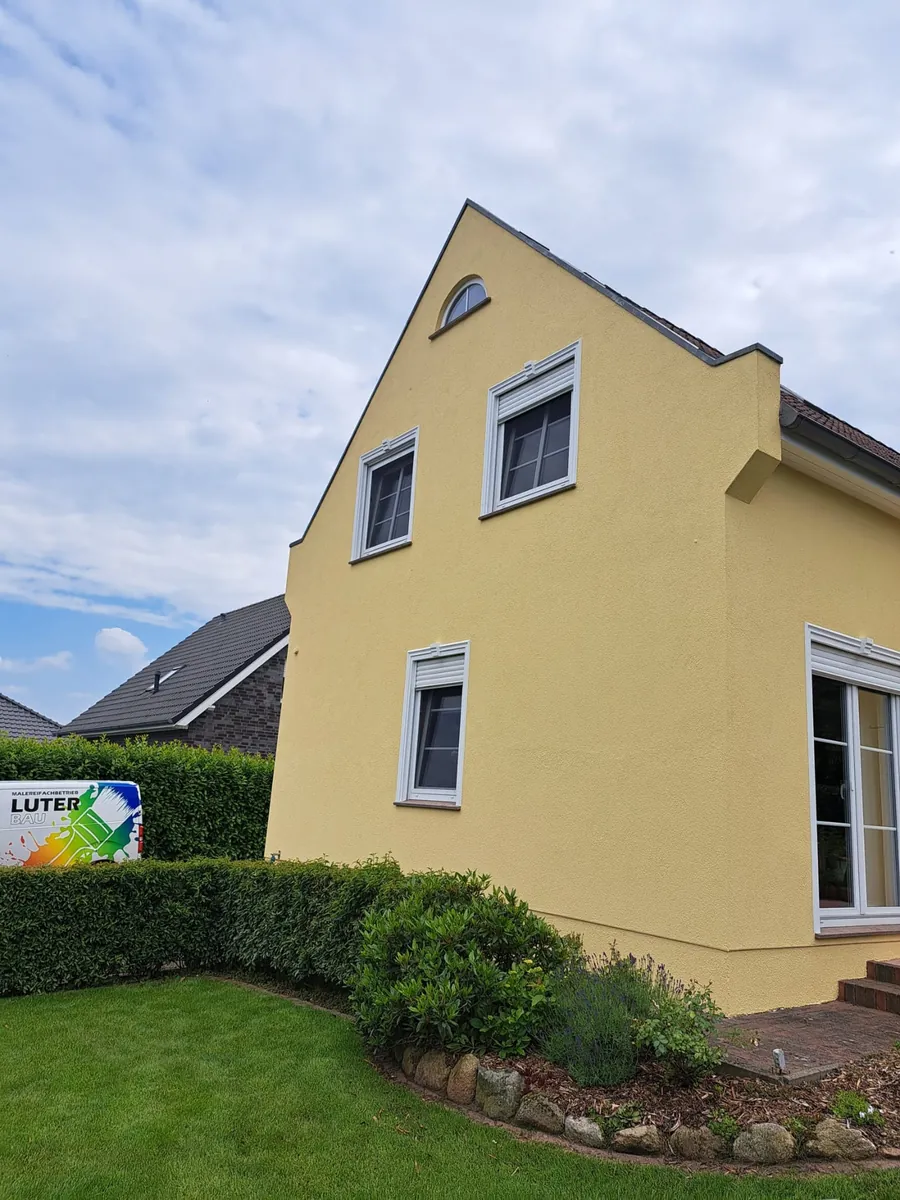 Einfamilienhaus mit frisch gestrichener gelber Fassade und angelegtem Vorgarten